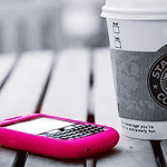 Розовый сотовый телефон и стакан кофе