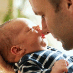 Малыш, лежащий на руке отца, целует его в нос